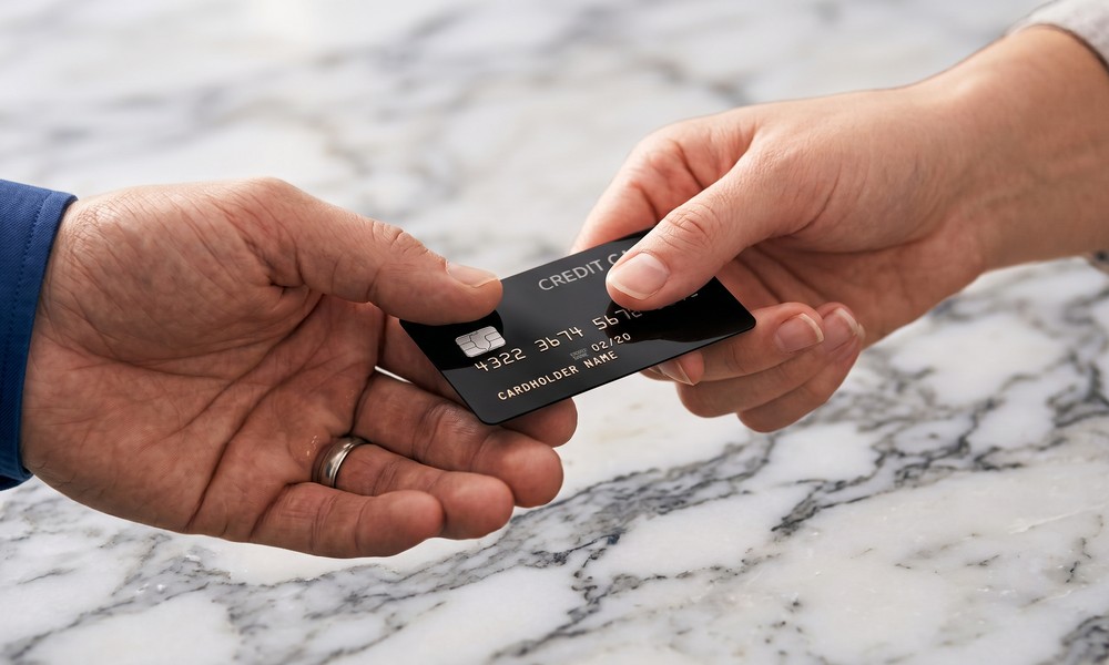 Close-up of one hand passing a black credit card to another hand over a marble countertop. Close-up of one hand passing a black credit card to another hand over a marble countertop.