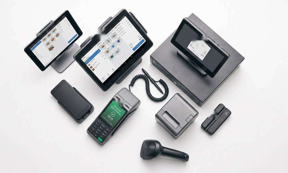 A lineup of point-of-sale payment terminals and card readers of different sizes — handheld devices, a countertop terminal with receipt printer, a tablet POS with barcode scanner — arranged on a white background. A lineup of point-of-sale payment terminals and card readers of different sizes — handheld devices, a countertop terminal with receipt printer, a tablet POS with barcode scanner — arranged on a white background.